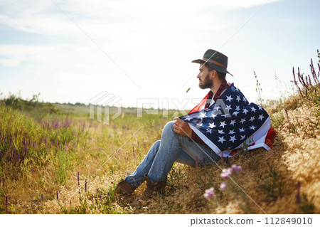 4th of July. American Flag. Traveler with the flag of America. The man in a hat, a backpack, a shirt and jeans. 4th of July. American Flag. Traveler with the flag of America. The man in a hat, a backpack, a shirt and jeans. 112849010