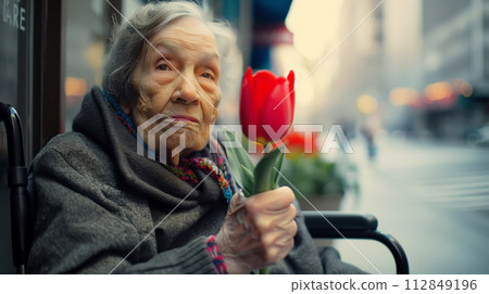 AI-generated content. An elderly woman with Parkinson's disease and red tulip in his hands in wheelchair on city street 112849196
