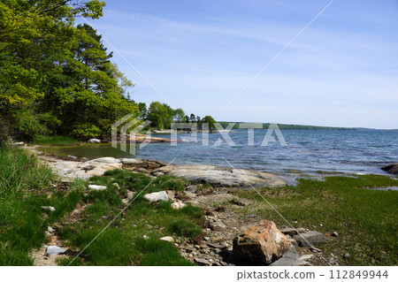 Rocky coastline with pier in distance and green trees on Littlejohn Island 112849944