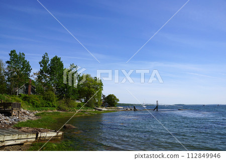 Rocky coastline with pier in distance and green trees 112849946