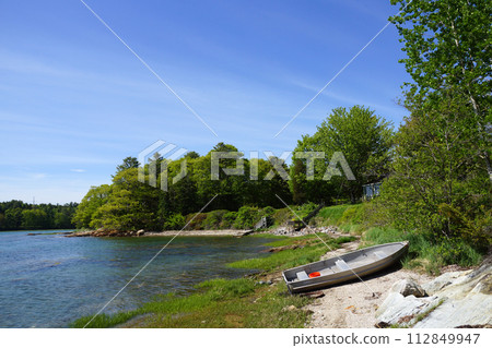 Rocky coastline with metal boat on shore and lined with green trees 112849947