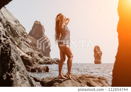 Woman summer travel sea. Happy tourist enjoy taking picture outdoors for memories. Woman traveler posing on the beach at sea surrounded by volcanic mountains, sharing travel adventure journey Woman summer travel sea. Happy tourist enjoy taking picture outdoors for memories. Woman traveler posing on the beach at sea surrounded by volcanic mountains, sharing travel adventure journey 112854744
