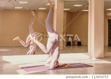 Young sporty woman, fitness instructor in pink sportswear doing stretching and pilates on yoga mat in the studio with mirror. Female fitness yoga routine concept. Healthy lifestyle and harmony. Young sporty woman, fitness instructor in pink sportswear doing stretching and pilates on yoga mat in the studio with mirror. Female fitness yoga routine concept. Healthy lifestyle and harmony. 112854757