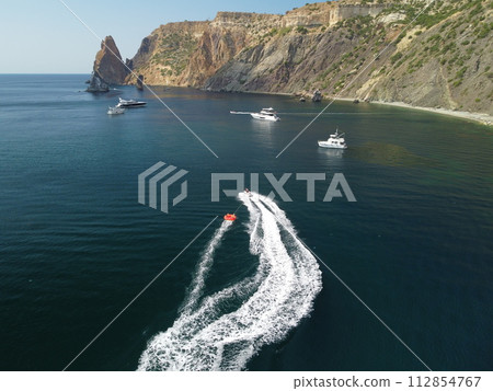 Happy people swim on air mattress behind a high speed water bike. Tourists ride on inflatable watercraft boat. Sea attraction. Water scooter skating people on large Inflatable raft. Slow motion 112854767