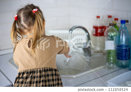 A child sorts plastic bottles in the kitchen. A little girl painstakingly puts plastic into containers for recycling. A family of environmental activists sorts garbage and fights to save the planet. A child sorts plastic bottles in the kitchen. A little girl painstakingly puts plastic into containers for recycling. A family of environmental activists sorts garbage and fights to save the planet. 112858524