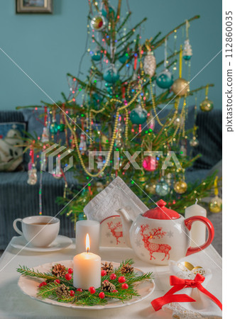 New Year's tea party at the table with a teapot, candles on the background of the Christmas tree 112860035