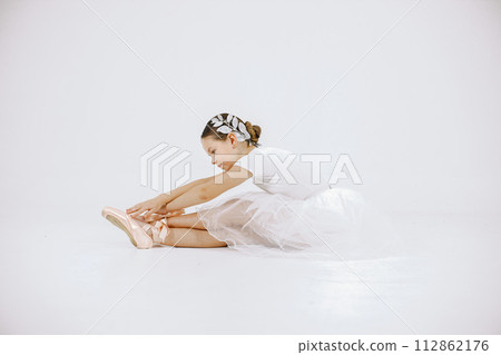 Little ballerina on white background. Brunette girl wearing white ballet suit. Girl sitting on a floor. Little ballerina on white background. Brunette girl wearing white ballet suit. Girl sitting on a floor. 112862176