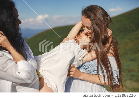 Stylish family in the mountains. Grandma with daughter and granddaughter on a sky background. Woman in a white dress. Stylish family in the mountains. Grandma with daughter and granddaughter on a sky background. Woman in a white dress. 112862220