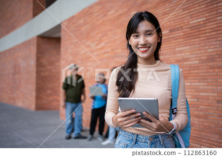 Young and cute Asian college student girls smile carrying a backpack with a textbooks in front of the university campus building. learning materials, importance of education becoming intelligent Young and cute Asian college student girls smile carrying a backpack with a textbooks in front of the university campus building. learning materials, importance of education becoming intelligent 112863160