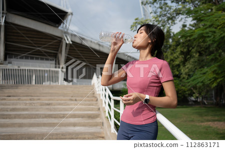 Happy healthy woman drinking water from bottle after workout exercise. Sports, nutrition bottle, and female athletes drink liquid for hydration after exercising, a Healthy and active lifestyle 112863171