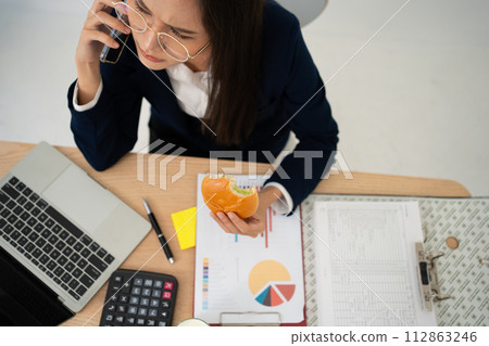 Busy and tired businesswoman eating Bread and milk for lunch at the Desk office and working to deliver financial statements to a boss. Overworked and unhealthy for ready meals, burnout concept. 112863246