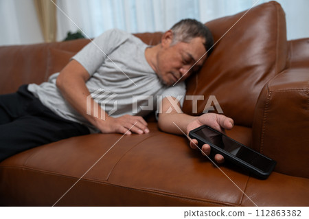 Senior male asian presses hand to his chest has a heart attack suffers from unbearable pain in the living room, lonely men try using the smartphone to call for Emergency help. Senior male asian presses hand to his chest has a heart attack suffers from unbearable pain in the living room, lonely men try using the smartphone to call for Emergency help. 112863382