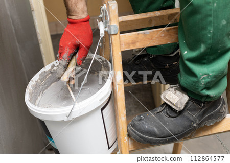 A close up shows how a manual worker soaks a paint roller in a bucket with moisture insulation. Protective glove. 112864577