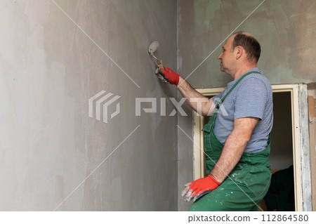 In the bathroom, a general construction worker applies moisture insulation using a roller. In the bathroom, a general construction worker applies moisture insulation using a roller. 112864580