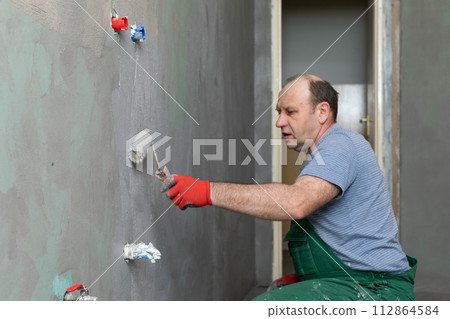 In the bathroom, a general construction worker applies moisture insulation using a roller. In the bathroom, a general construction worker applies moisture insulation using a roller. 112864584
