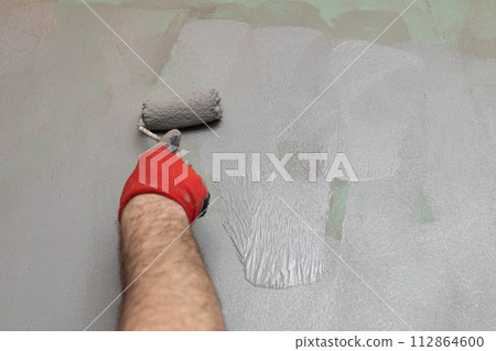A close-up view of an experienced construction worker applying damp insulation using a paint roller on a wall. A close-up view of an experienced construction worker applying damp insulation using a paint roller on a wall. 112864600