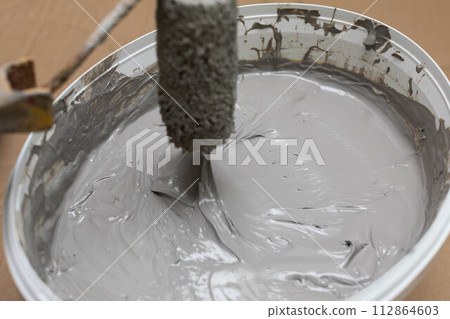 A close up shows how a manual worker soaks a paint roller in a bucket with moisture insulation. Protective glove. A close up shows how a manual worker soaks a paint roller in a bucket with moisture insulation. Protective glove. 112864603