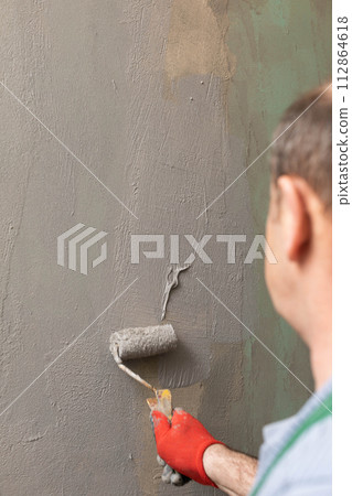In the bathroom, a general construction worker applies moisture insulation using a roller. 112864618
