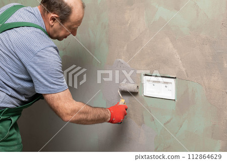 In the bathroom, a general construction worker applies moisture insulation using a roller. In the bathroom, a general construction worker applies moisture insulation using a roller. 112864629