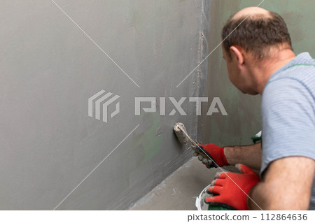In the bathroom, a general construction worker applies moisture insulation using a roller. In the bathroom, a general construction worker applies moisture insulation using a roller. 112864636
