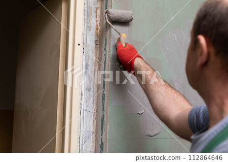 In the bathroom, a general construction worker applies moisture insulation using a roller. In the bathroom, a general construction worker applies moisture insulation using a roller. 112864646