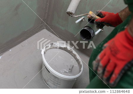 A professional worker soaks a paint roller in a bucket with moisture insulation. Protective glove. A professional worker soaks a paint roller in a bucket with moisture insulation. Protective glove. 112864648