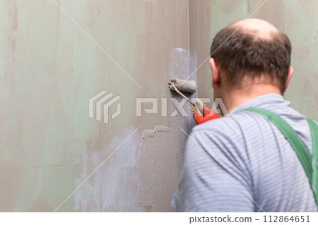 In the bathroom, a general construction worker applies moisture insulation using a roller. In the bathroom, a general construction worker applies moisture insulation using a roller. 112864651