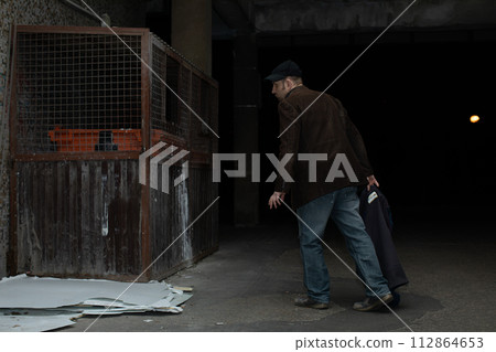 A middle-aged homeless man has found garbage cans and is heading towards him. A middle-aged homeless man has found garbage cans and is heading towards him. 112864653