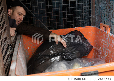 A middle-aged homeless man looks for treasures in the dustbin. A middle-aged homeless man looks for treasures in the dustbin. 112864655
