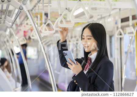 Image of a female high school student commuting to school by train looking at her smartphone screen 112866627