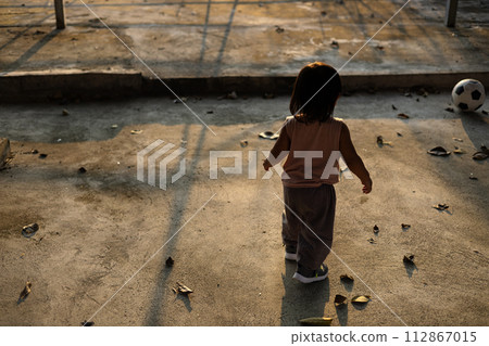 Asian boy plays football on the cement ground. boy plays in the outdoor taken from the back side. Asian boy plays football on the cement ground. boy plays in the outdoor taken from the back side. 112867015