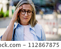 A woman wearing glasses is shown holding her head in this straightforward image. 112867875