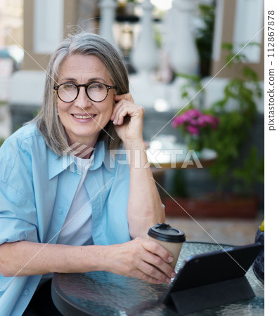A woman sits at a table, holding a cup of coffee in front of her. 112867878