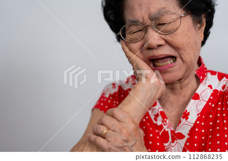Asia old senior woman suffering from severe toothache, holding her cheek and suffering strong dental pain on white background, tooth decay, tooth sensitivity, oral health care concept. 112868235
