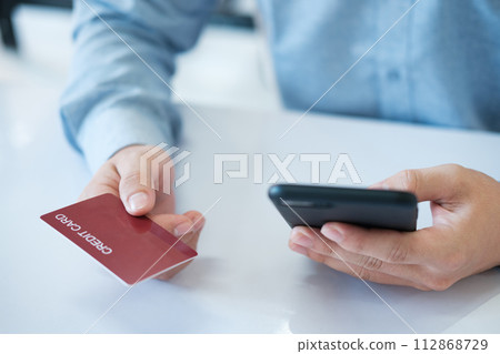 A man is using his phone to pay for something with a credit card A man is using his phone to pay for something with a credit card 112868729