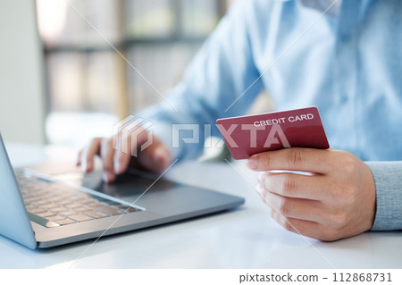 A man is using a laptop to pay for something with a red credit card A man is using a laptop to pay for something with a red credit card 112868731
