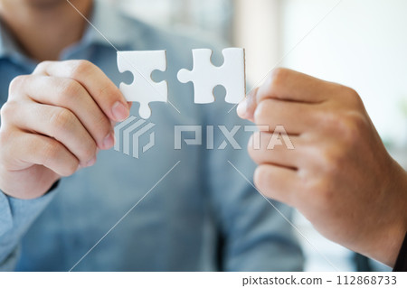 Two people holding a puzzle piece together. Concept of teamwork and collaboration. Two people holding a puzzle piece together. Concept of teamwork and collaboration. 112868733