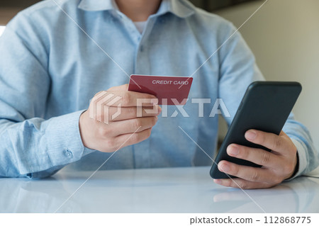 A man is using his phone to pay for something with a credit card A man is using his phone to pay for something with a credit card 112868775
