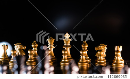 Golden chess pieces in dramatic backlighting Golden chess pieces in dramatic backlighting 112869985