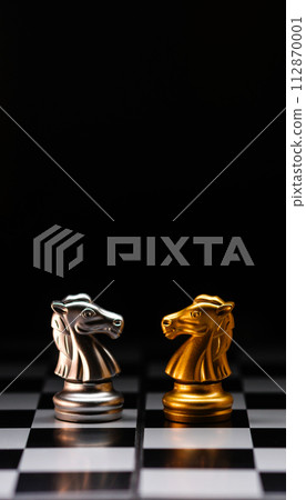Chess knights face-off. Silver and gold chessmen on chesboard. Chess knights face-off. Silver and gold chessmen on chesboard. 112870001
