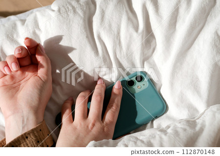 Hand holding smartphone on bed Hand holding smartphone on bed 112870148