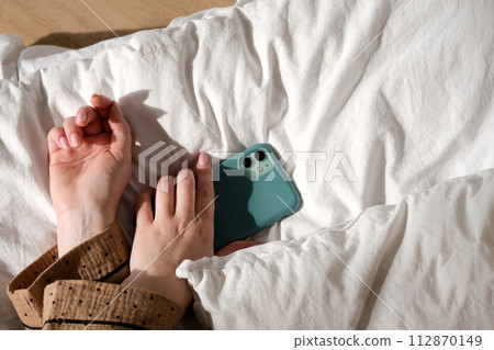 Hand holding smartphone on bed Hand holding smartphone on bed 112870149