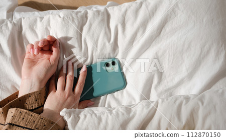 Hand holding smartphone on bed Hand holding smartphone on bed 112870150
