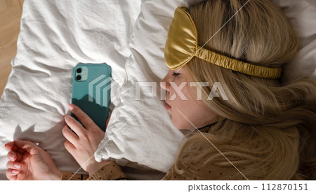 Woman asleep with phone, wearing eye mask Woman asleep with phone, wearing eye mask 112870151