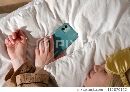 Woman asleep with phone, wearing eye mask 112870152
