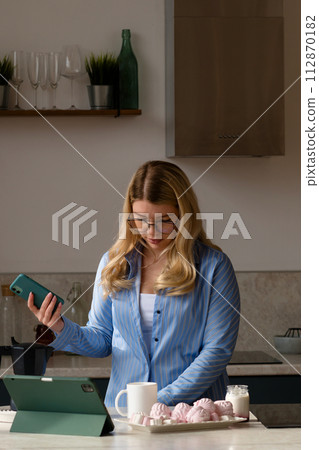 Woman using phone in kitchen with coffee Woman using phone in kitchen with coffee 112870182