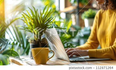woman sitting at wooden table and working on laptop. A cup of coffee with a potted plant. The environment is bright and clean, a relaxed work environment woman sitting at wooden table and working on laptop. A cup of coffee with a potted plant. The environment is bright and clean, a relaxed work environment 112871264