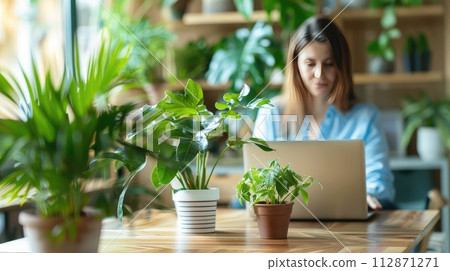 woman sitting at wooden table and working on laptop. A cup of coffee with a potted plant. The environment is bright and clean, a relaxed work environment woman sitting at wooden table and working on laptop. A cup of coffee with a potted plant. The environment is bright and clean, a relaxed work environment 112871271
