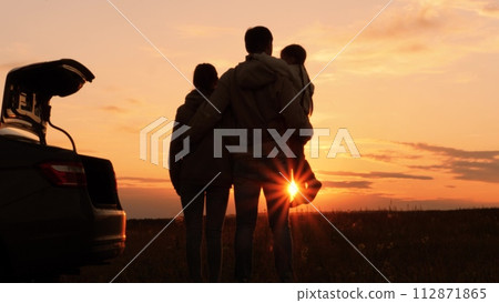 Silhouettes of happy family at sunset near car. Dad mom and girl kid watching contemplating setting sun, orange stunning summer sky. Solitude of family in nature, break from hustle and bustle of city Silhouettes of happy family at sunset near car. Dad mom and girl kid watching contemplating setting sun, orange stunning summer sky. Solitude of family in nature, break from hustle and bustle of city 112871865