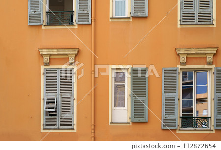 France. Cannes. Beautiful wooden windows with shutters. Beautiful wooden window shutters with window sill, orange cement wall on a sunny day 112872654